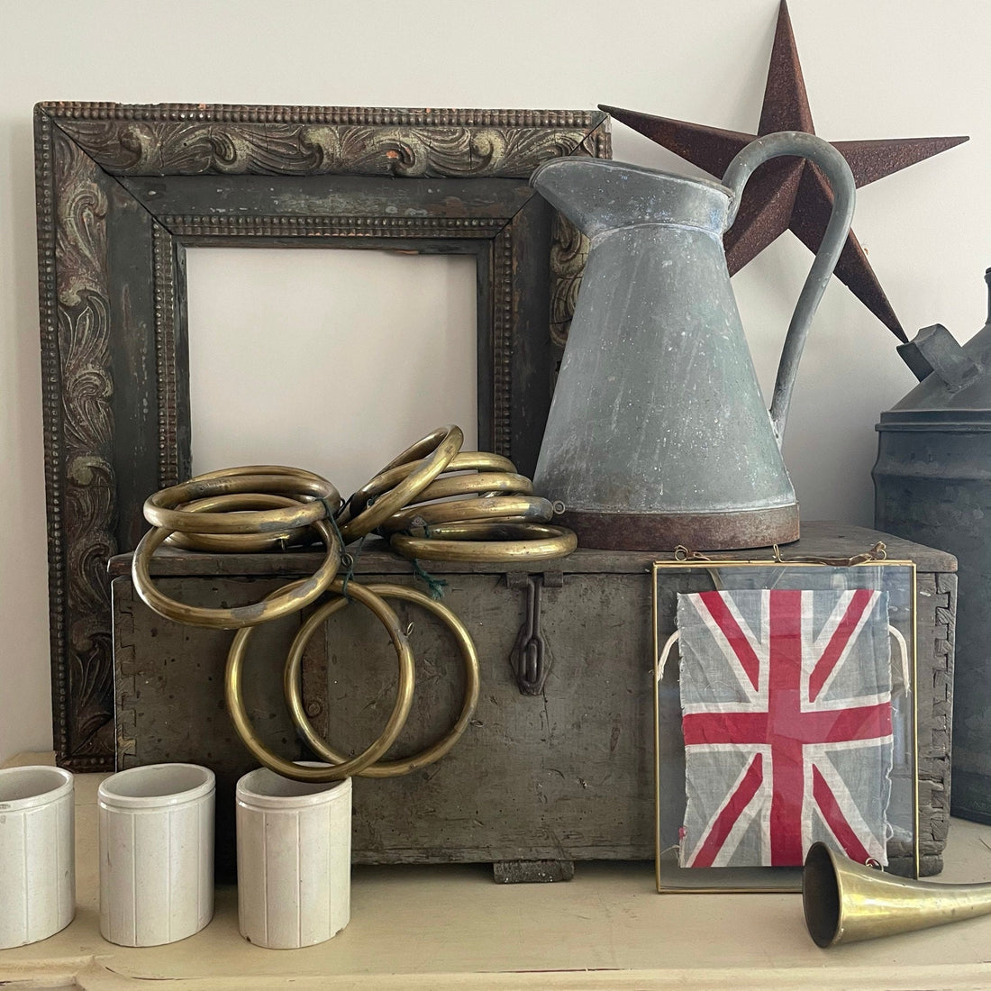 an eclectic mix of vintage and antique items, a collection of curated vintage telling a story of the home, a vintage union jack in brass frame, picks up on the antique hunting horn and beautiful oversized brass curtain rings. 